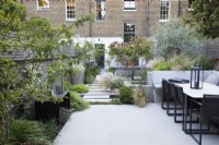 Dining area at the end of the city garden, bordered with Stipa tenuissima, olive tree, Pittosporum tobira 'Nanum' and Verbena bonariensis, with clumps of Hakonechloa macra by the folded metal table