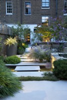 In the evening, the outdoor lighting picks up details of the sunken pond, water feature, stepping stones and Astelia chathamica planted in pots and Pittosporum tobira 'Nanum'