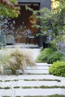 The planting by the path of sandstone paving stones leading to the zinc clad building includes Stipa tenuissima and Verbena bonariensis on the left and Pittosporum tobira 'Nanum' and Hakonechloa macra on the right with Thymus praecox 'Albiflorus' running between the paving stones.