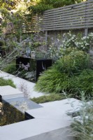 The planting by the metal folded table includes Hakonechloa macra, Euphorbia mellifera, Trachelospermum jasminoides climbing against the wall and Athyrium nipocum 'Pewter Lace'