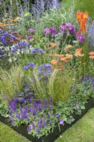 Corner of a metal raised bed filled with flowering perennials such as Agapanthus and Achillea along with ornamental grasses, July