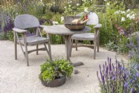 Seating area with wooden table, two chairs and inset herb planter surrounded by summer border planted with perennials and ornamental grasses. RHS Iconic Horticultural Hero Garden, Designer: Carol Klein, RHS Hampton Court Palace Garden Festival 2023