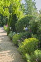 View along a gravel path next to a mixed border with herbaceous perennials, clipped shrubs roses and yew topiary. June.
