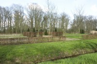 Overview with topiary trees between large pruned hedges Fagus Sylvatica in a block shape. Ditch in the foreground.