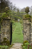 Entrance into the walled garden at Cerney House in March with gate posts topped with pineapple finials