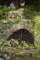 Metal grill below a stone lion at Cerney House Gardens in March