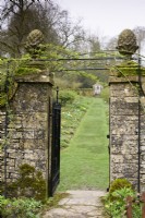 Entrance into the walled garden at Cerney House in March with gate posts topped with pineapple finials
