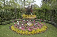 Urn with cordyline and ornamental grasses standing in a circular island flowerbed with an arrangement of pink and white tulips and bellis ground cover, Avenue Gardens, The Regent's Park, London, UK 