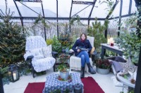 Woman reading magazine in large greenhouse decorated with fairy lights and mixed plants