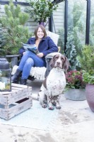 Dog sitting by woman on chair with magazine in inside decorated greenhouse