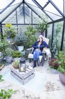 Woman sitting on chair with hot drink inside decorated greenhouse