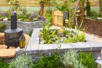 Mini raised pond with Connemara cap stones and picnic area with modern chiminea. Planted with Helichrysum italicum, Equisetum hyemale, aquatic plants in a woodland inspired garden. June
Designer: Mary Anne Farenden. Bord Bia Bloom, Super Garden, Dublin, Ireland.