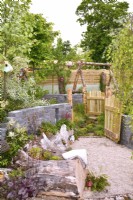 Rustic woodland inspired garden with a large tree stump used as a flowerbed and seating area, open wooden gates leading to different area. Planted with  Astilbe koreana,  Pyrus salicifolia, Betula pendula. June
Designer: Mary Anne Farenden. Bord Bia Bloom, Super Garden, Dublin, Ireland.