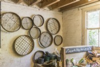 Collection of vintage garden sieves and riddles hanging on the wall next to a potting bench.