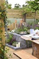 Rustic woodland inspired garden surrounded by a wooden planks fence with raised bed  made of Connemara decorative wall system. Planted with Thymus vulgaris, Leucanthemum superbum, Salvia Nemorosa, Sorbus aria. June
 


