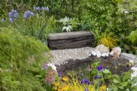 Small pond bordered by bed of perennials such as primula, iris, rodgersia, acer palmatum and agapantus in the 'Greener Pastures' garden at BBC Gardener's World Live 2015, June