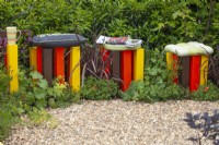 Yellow, brown and red posts with cushions for seating in bed containing Phormium and Alchemilla mollis in the 'In the Loop' garden at BBC Gardener's World Live 2015