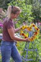 Placing a wreath made of summer flowers including Helianthus, Coreopsis, Calendula, Foeniculum and Achillea on top of wooden obelisk.