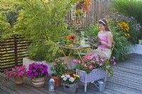 Colourful summer terrace with bedding flowers in containers, a girl enjoys reading a magazine.