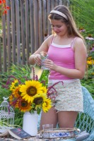 Summer flower bouquet with sunflowers, girl pours cold drink into a glass.