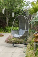 A hanging outdoor garden chair with grey cushions in a small contemporary garden. June.
