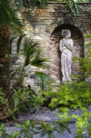 View into semi tropical 'secret' garden with Tree Ferns , Acer palmatum and palms, classical statue set in to stone wall