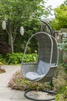 A hanging outdoor garden chair with grey cushions in a small contemporary garden. June.