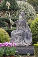 Statue of Britannia with latin inscription and terracotta pots with tulips. Topiary of Yew behind. April. Spring. 