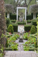 View into the Silver Jubilee Garden and the Rose Garden beyond. Low clipped hedge of Box and Yew. Armillary on pedestal. Tulips in borders. April. Spring. 