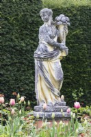 Classical statue of woman carrying basket of flowers. April. Spring.