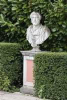 Bust on plinth with hedge of Laurel behind and clipped hedge of Yew by the Colonnade Court. April. Spring. 
