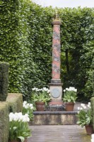 The Elizabeth I and II crowned column backed by Laurel hedge.  Terracotta pots planted with Tulipa 'Virgin Queen' and contained by hedges of clipped Yew. April. Spring. 