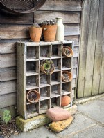 Rustic wooden shelving unit against a shed with small terracotta pots filled with succulents