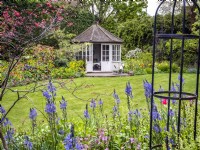 A country garden in spring with a central summerhouse surrounded by borders of mixed planting including camassia leichtlinii, Silene dioica, Tellima grandiflora, tulips and a metal obelisk