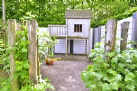 Painted white wooden  playhouse for children in the corner of the private garden by a fence. May