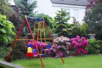 Colorful childrens swing  on a lawn in spring garden with Azaleas.